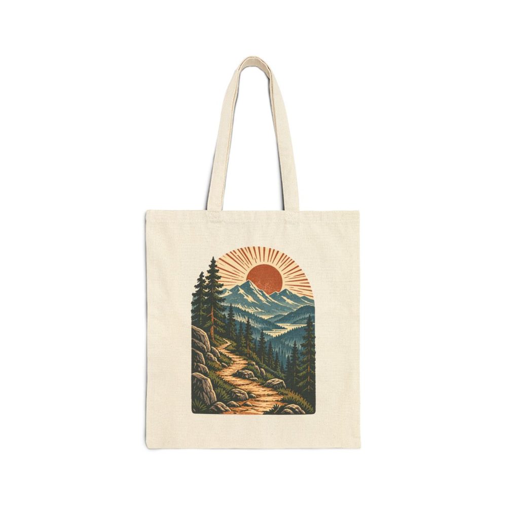 Mountain Trail tote bag in natural cotton canvas, printed with a winding trail through cedar trees toward layered blue mountains and a rising sun